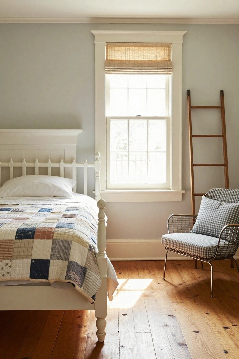 Light gray bedroom with white spindle bed draped in colorful patchwork quilt, tall wooden ladder leaning near window with bamboo shade, wire chair with check pillow, and pine wood floors.