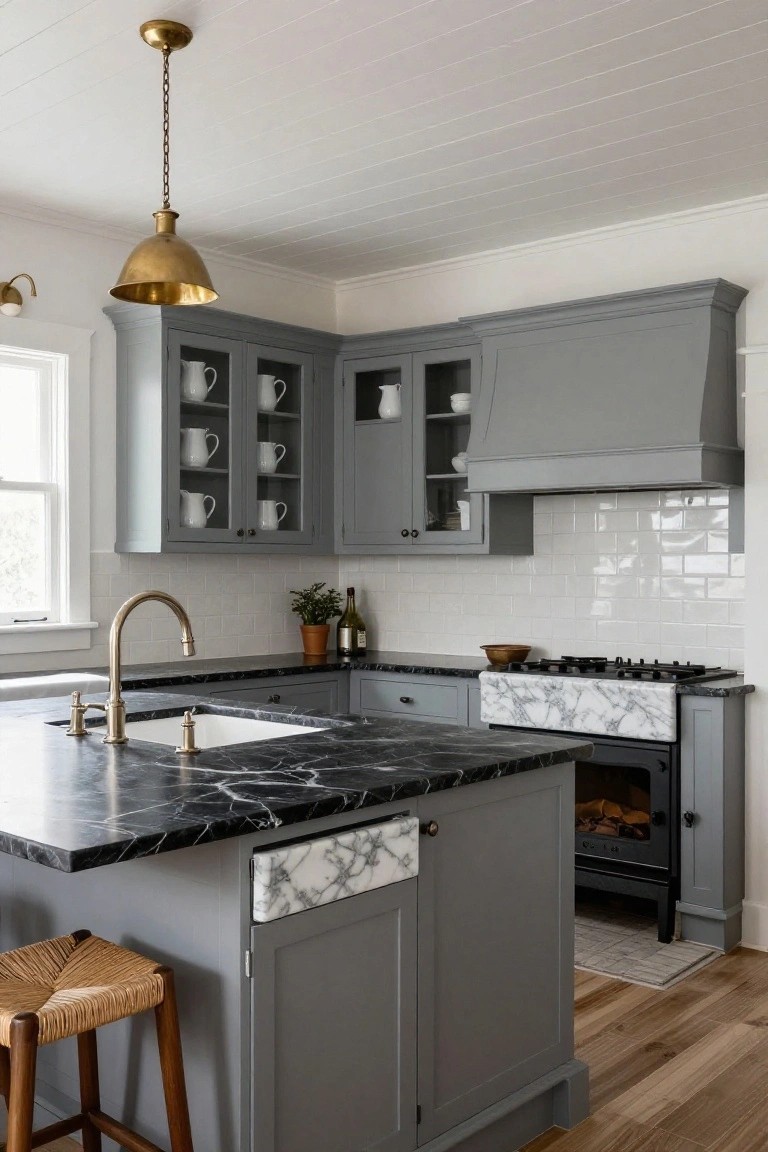 Corner kitchen interior with gray shaker cabinets, black marble countertops and island, white farmhouse sink, brass gooseneck faucet, gas range, wood stools, and brass pendant light.