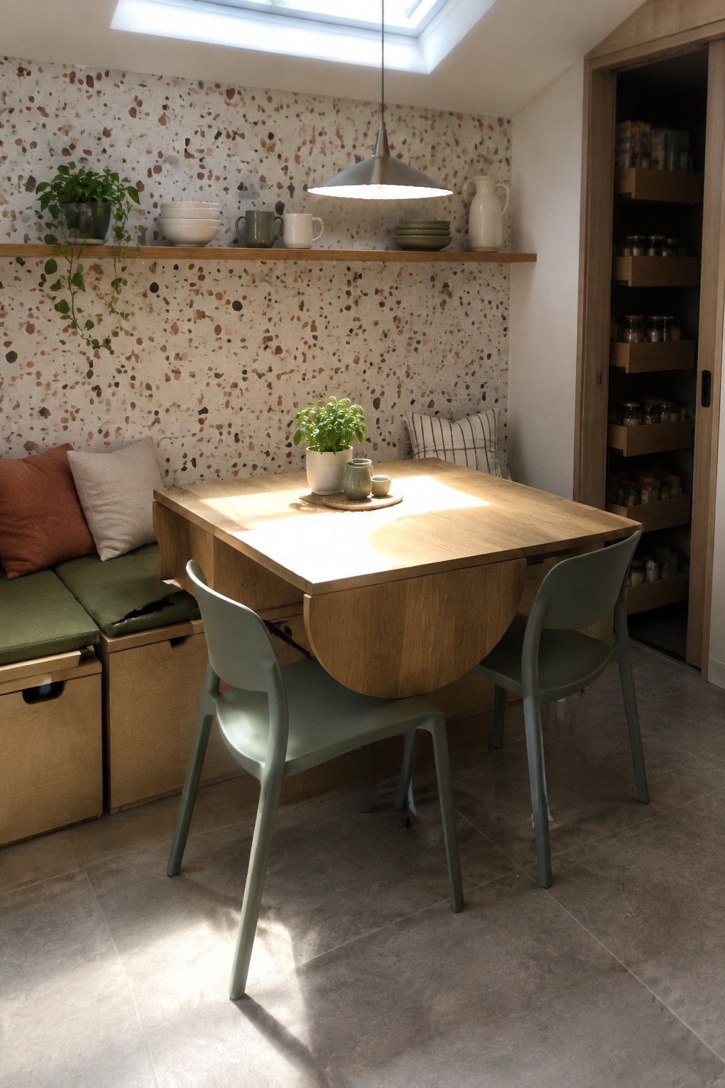 Sunlit wooden drop-leaf table with green chairs in terrazzo-walled dining nook