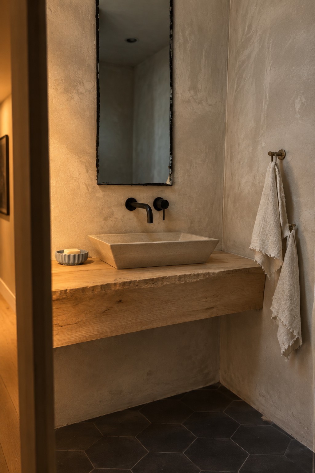 A bathroom interior with a floating wooden vanity slab holding a rectangular stone sink, black wall-mounted faucet, textured plaster walls, and a tall mirror above.