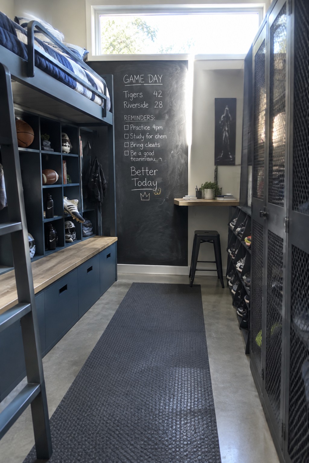 A narrow teen bedroom featuring a dark blue loft bed over built-in navy storage cubbies and drawers, a large chalkboard wall with sports scores and reminders, and metal lockers along the right wall.