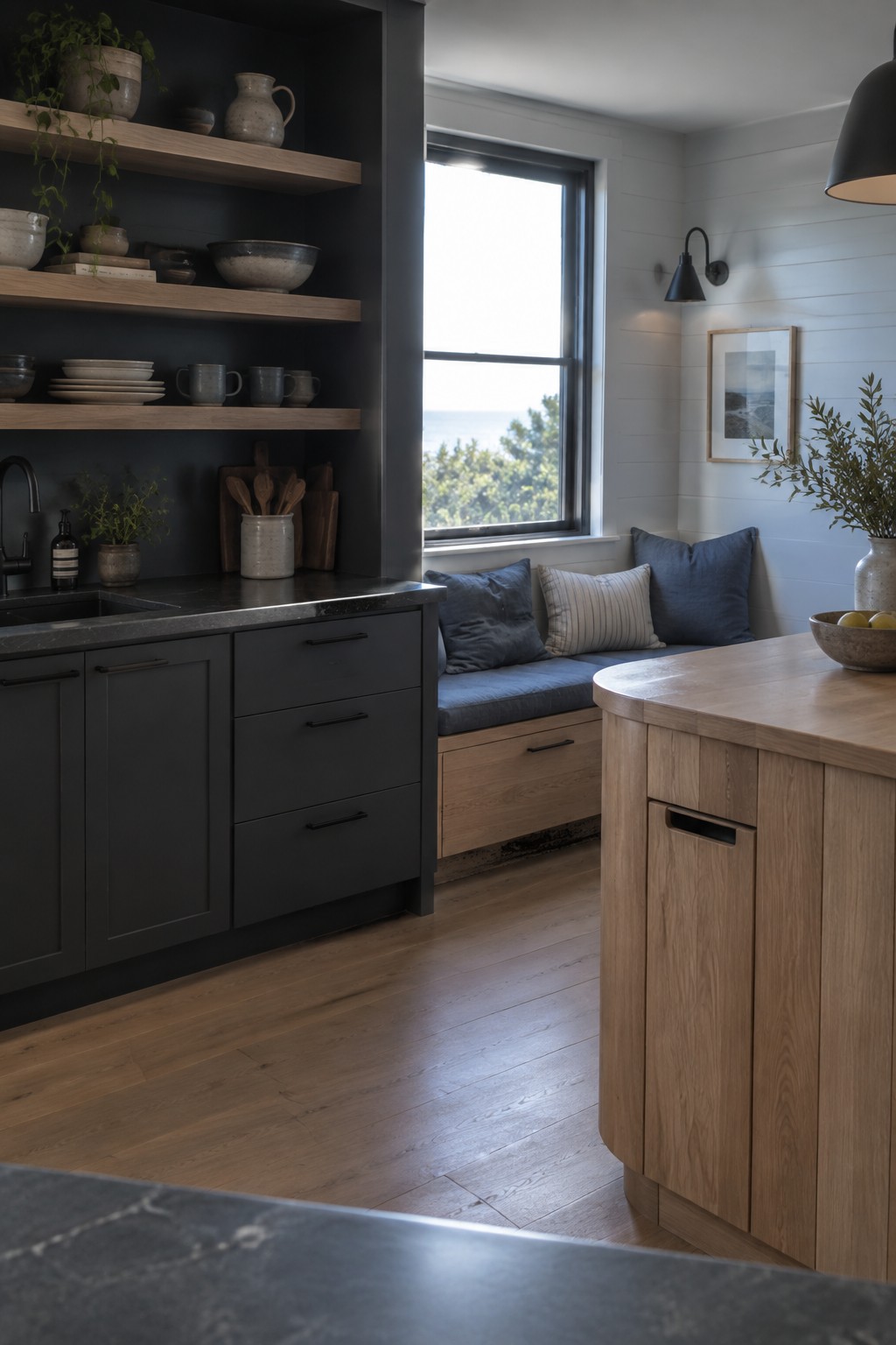 Modern kitchen with dark cabinets, wooden island, blue-cushioned window bench, and open pottery shelves.