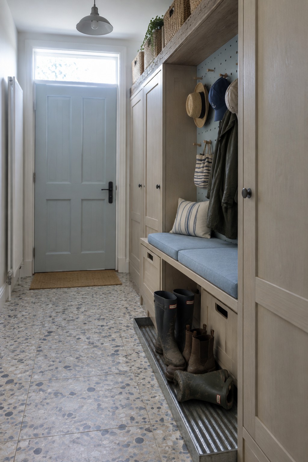 A light wood built-in mudroom with blue cushioned bench seating, pegboard above for hanging items, and open storage drawers beside a light blue door.