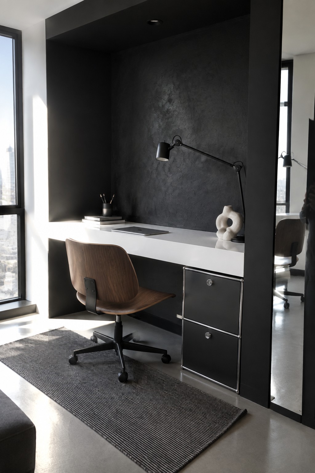 A white built-in desk sits recessed into a dark textured wall alcove, with a wooden office chair on a striped rug and black filing cabinets underneath.