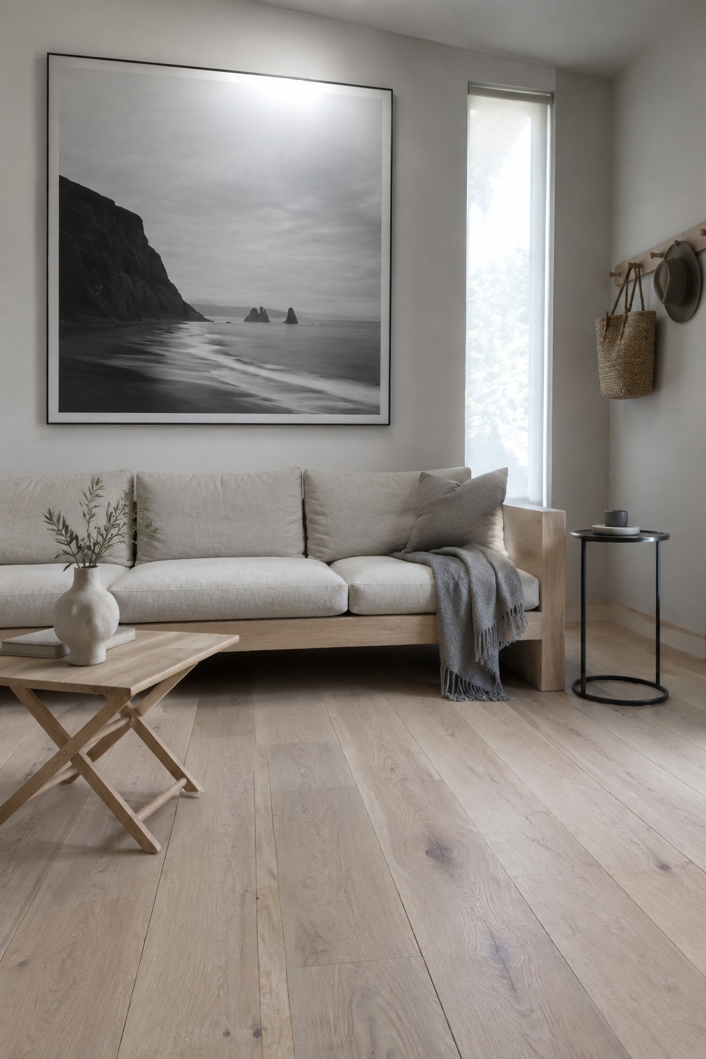 A living room with a large black and white landscape photograph hanging above a light beige sofa on a light wood floor.