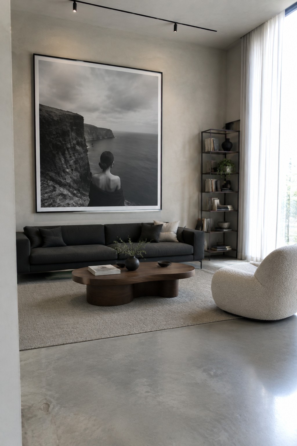 A modern living room with a large black and white photograph of a woman overlooking the ocean hanging above a dark gray sofa and wooden coffee table.