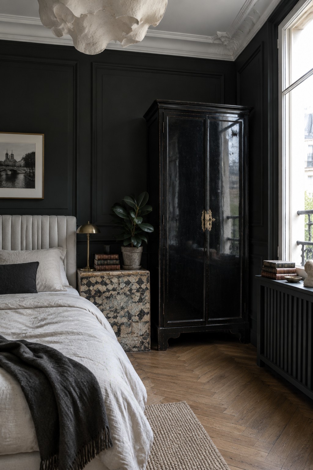 Dark elegant bedroom with white bed, black armoire, patterned nightstand, and herringbone floor