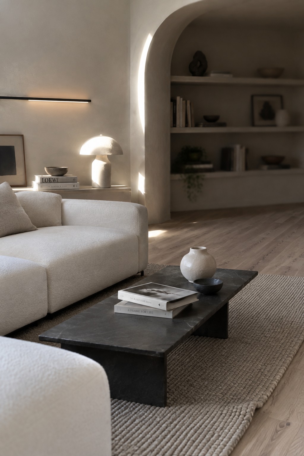 A modern living room with a white sectional sofa, dark marble coffee table on a woven rug, and arched built-in shelves in the background.