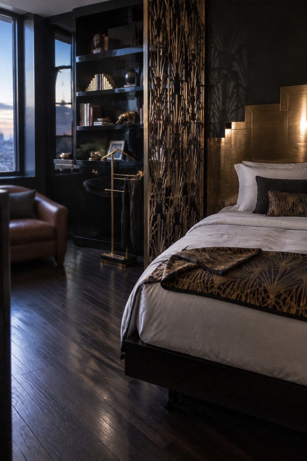 A bedroom featuring a large bed with a geometric brass headboard against dark walls, white bedding with gold patterns, and a tall decorative metal screen divider.