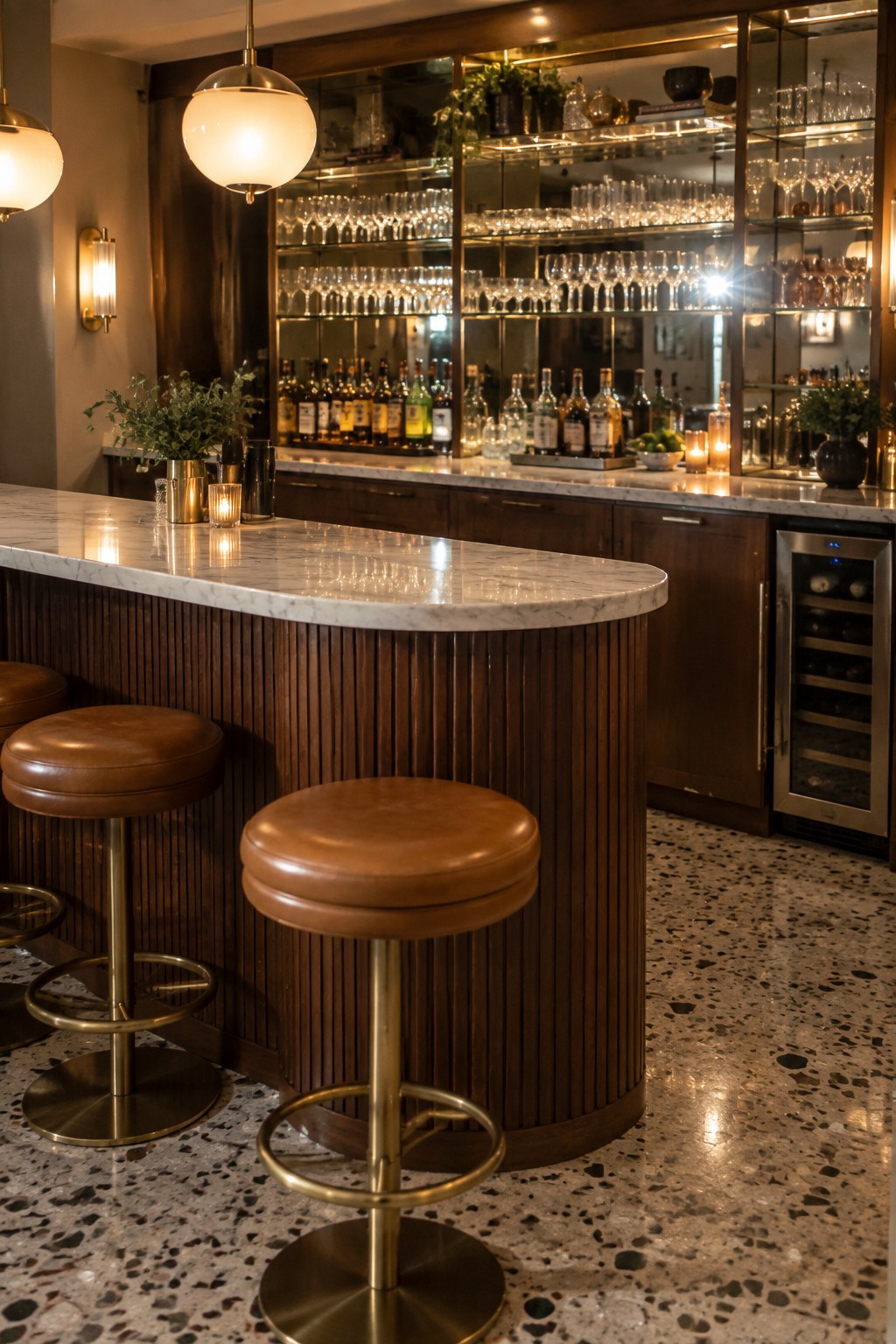 A curved home bar with white marble top, vertical wood slat base, brown leather stools, and backlit glass shelves holding bottles and glassware.