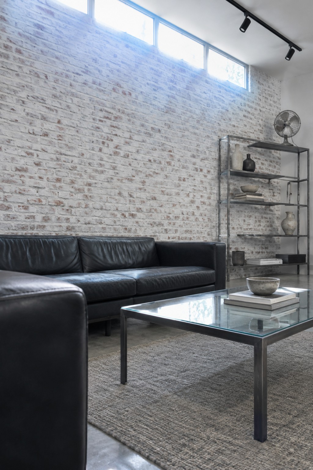 Modern living room with black leather sofa, glass coffee table, and white brick wall
