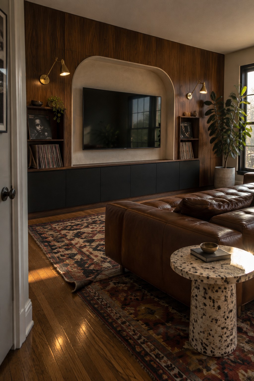 A living room featuring a flat-screen TV mounted inside an arched recessed niche on a dark wood paneled wall, with black built-in cabinets below and open shelves holding records on either side.