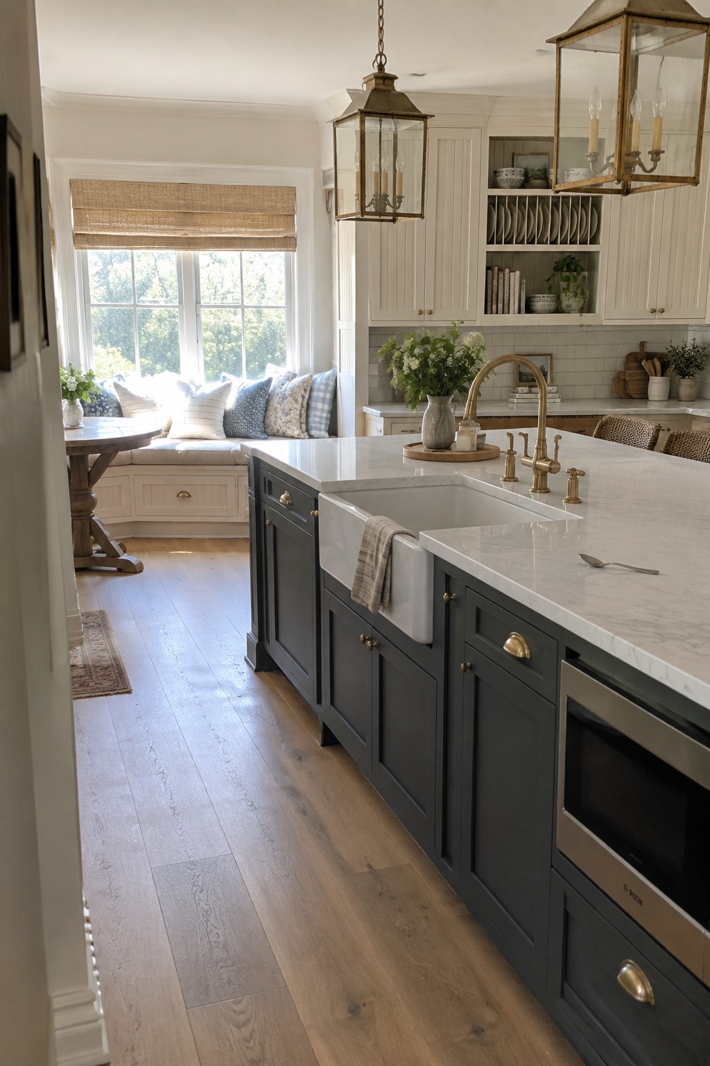 A kitchen interior showing white upper cabinets and dark gray lower cabinets with a white farmhouse sink and brass faucet.