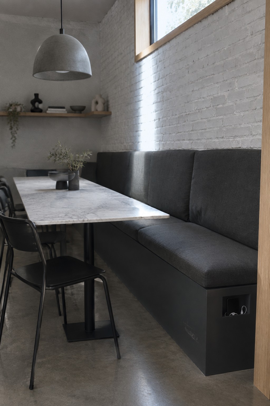 Modern dining area with marble table, black chairs, gray bench, and white brick wall