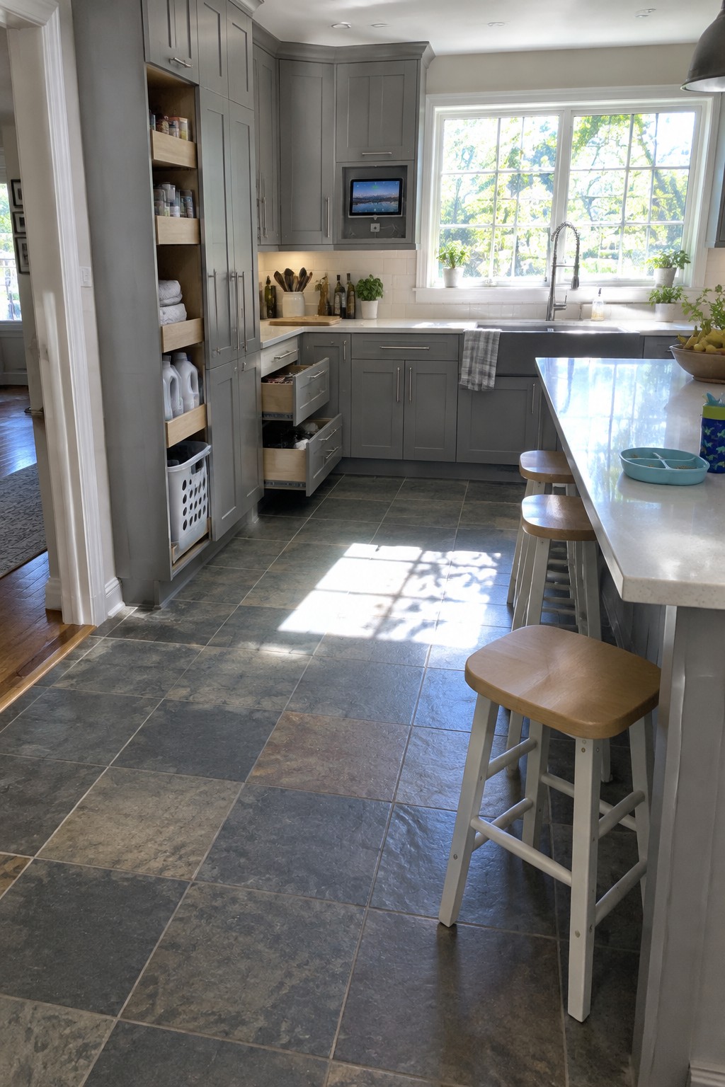 Modern gray kitchen with open drawers, wooden stools, white island, and sunlit floor