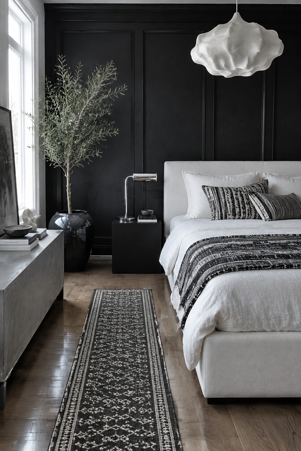 Modern bedroom with black walls, white bed, olive tree, cloud light, and runner rug.
